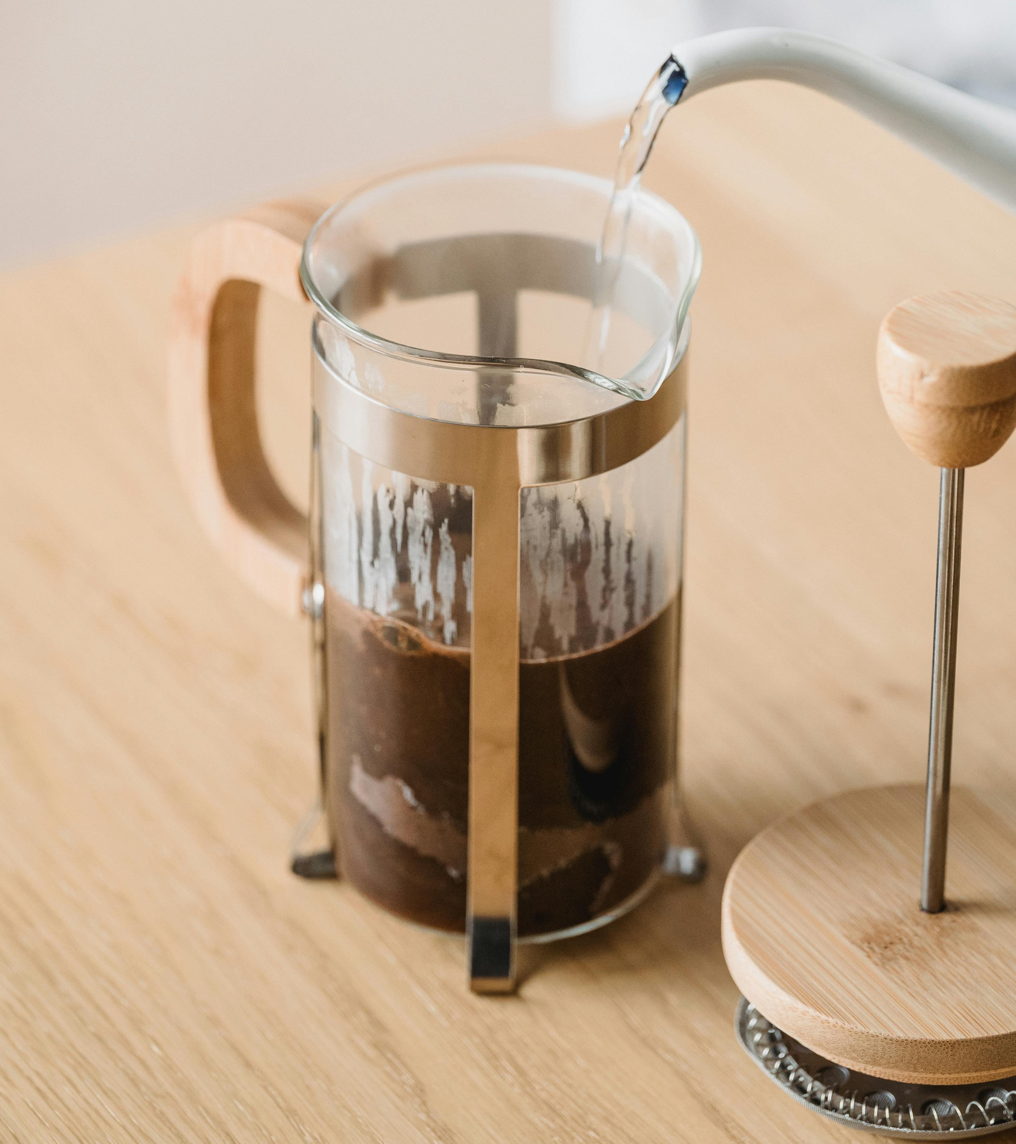 Brewing a french pressed coffee with a wooden top, using a white gooseneck kettle