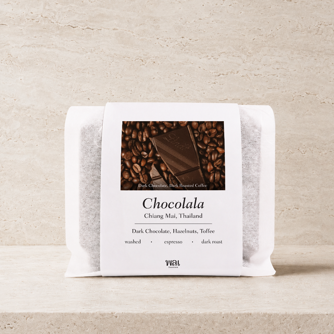 a bag of thai coffee beans in a translucent bag with a white paper sleeve with the words chocolala on it on a stone background and ledge made for espresso