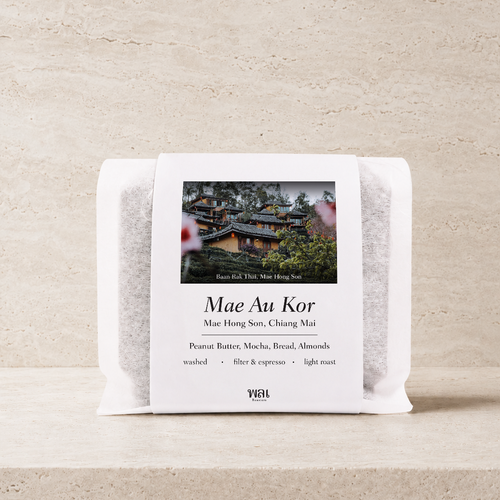 a bag of thai coffee beans in a translucent bag with a white paper sleeve with the words mae au kor on it on a stone background and ledge made for filtered and espresso coffee