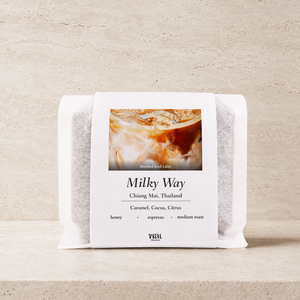 a bag of thai coffee beans in a translucent bag with a white paper sleeve with the words milky way on it on a stone background and ledge made for espresso