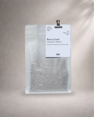 a bag of thai coffee from thailand in a translucent/transparent bag with llinen like texture, withy a meta bulldog clip holding a card on the bag with a grey background roasted for filter coffee
