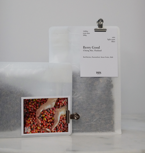 A transparent/translucent bag of light roast thai coffee beans from wai roasters with a card/postcard/polaroid clipped onto the bag roasted for filter brews
