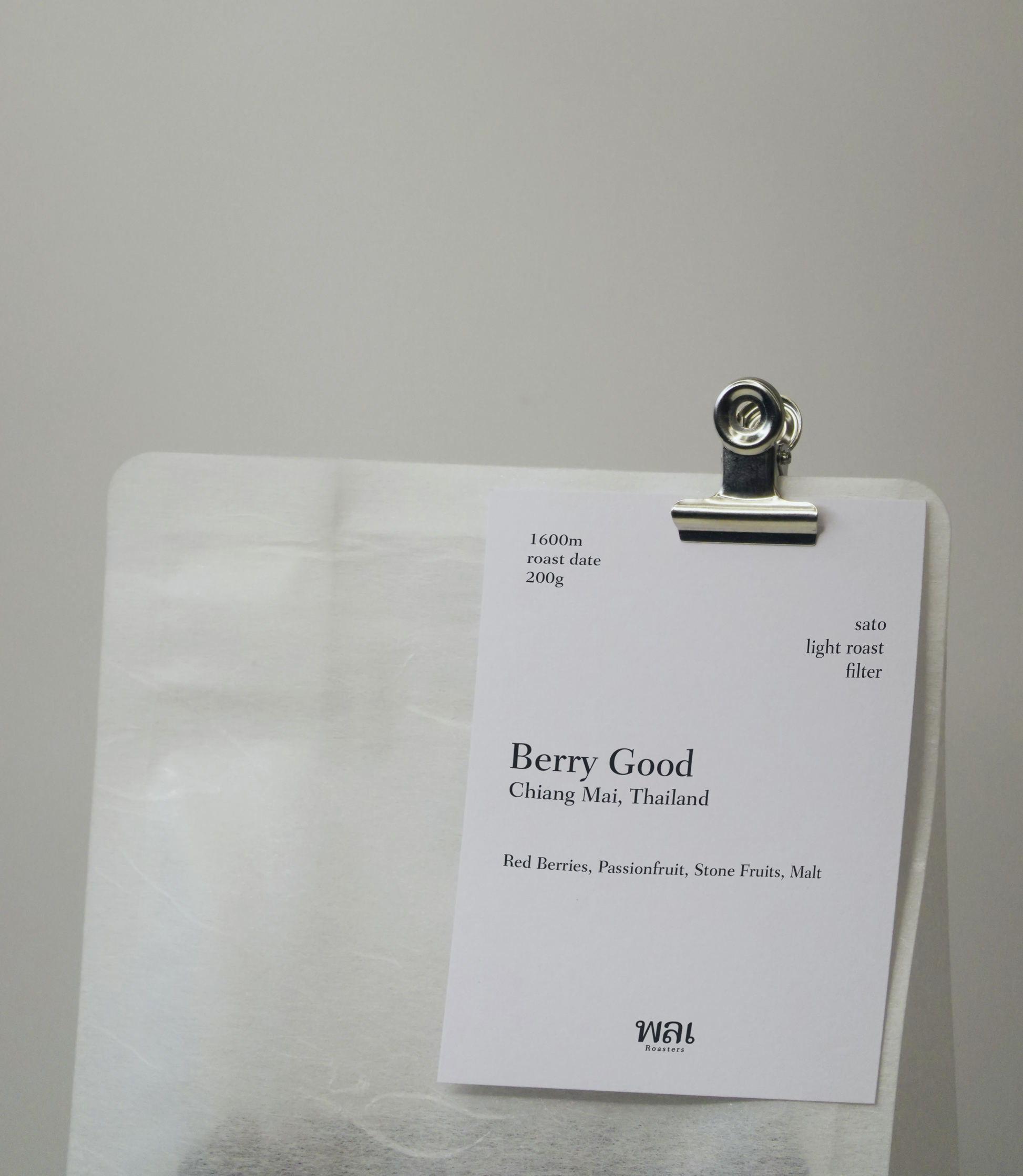 A transparent/translucent bag of light roast thai coffee beans from wai roasters with a card/postcard/polaroid clipped onto the bag roasted for filter brews
