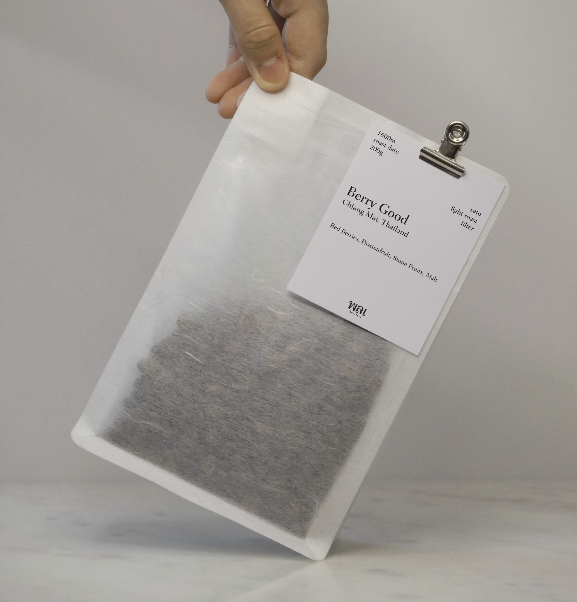 A transparent/translucent bag of light roast thai coffee beans from wai roasters with a card/postcard/polaroid clipped onto the bag roasted for filter brews
