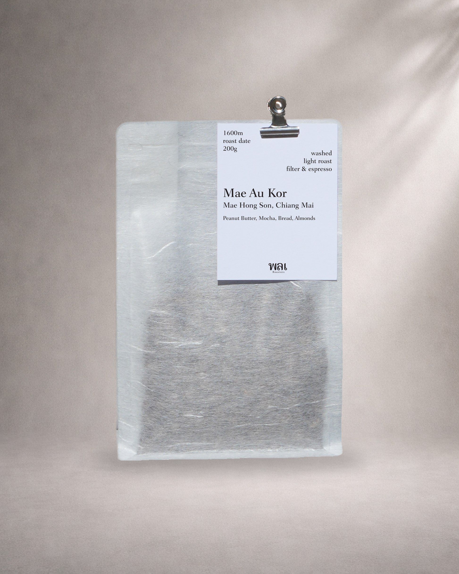 a bag of thai coffee from thailand in a translucent/transparent bag with llinen like texture, withy a meta bulldog cllip holding a card on the bag with a grey background roasted for filter and espresso coffee