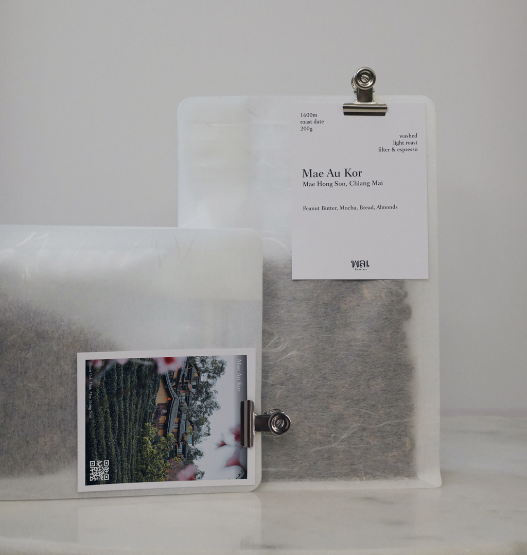 A transparent/translucent bag of light roast thai coffee beans from wai roasters with a card/postcard/polaroid clipped onto the bag roasted for filter brews