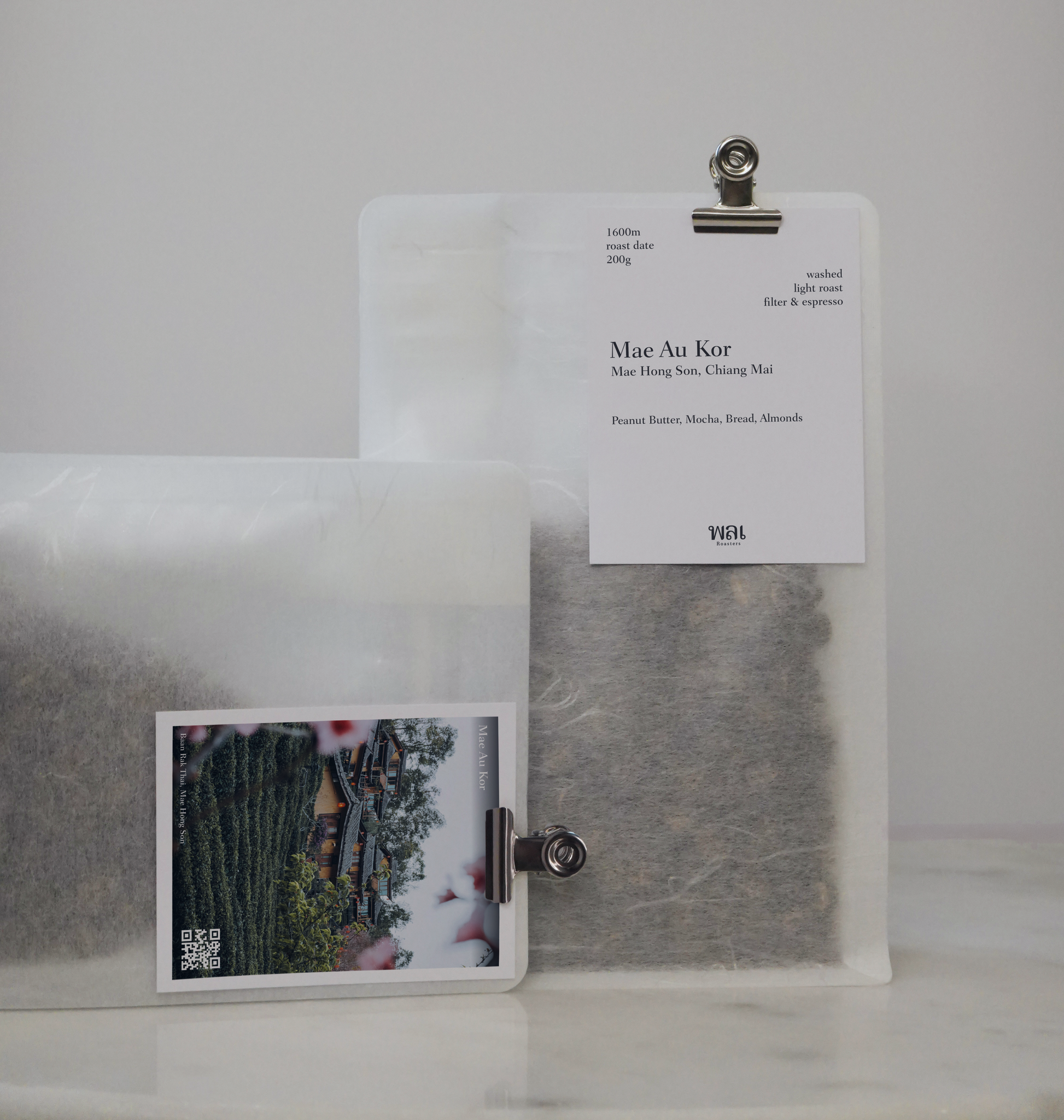 A transparent/translucent bag of light roast thai coffee beans from wai roasters with a card/postcard/polaroid clipped onto the bag roasted for filter brews