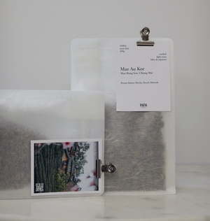 A transparent/translucent bag of light roast thai coffee beans from wai roasters with a card/postcard/polaroid clipped onto the bag roasted for filter brews