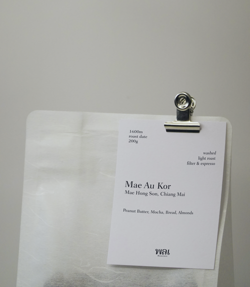 A transparent/translucent bag of light roast thai coffee beans from wai roasters with a card/postcard/polaroid clipped onto the bag roasted for filter brews