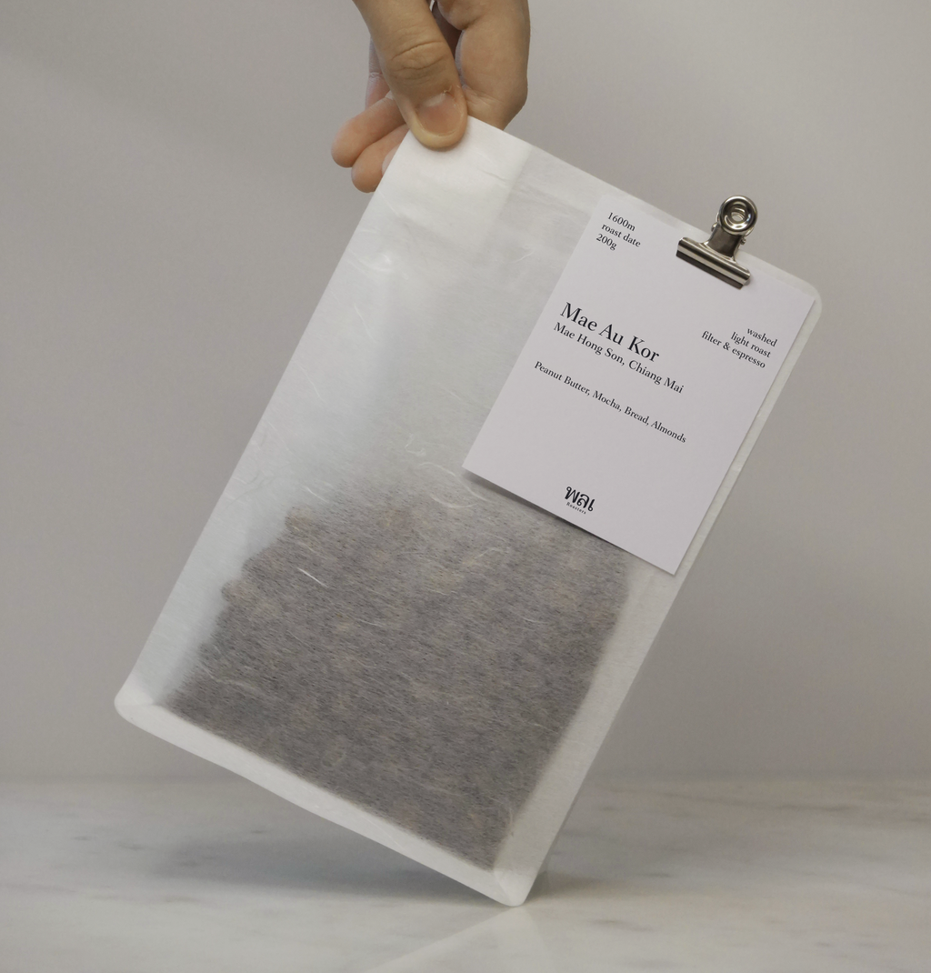 A transparent/translucent bag of light roast thai coffee beans from wai roasters with a card/postcard/polaroid clipped onto the bag roasted for filter brews