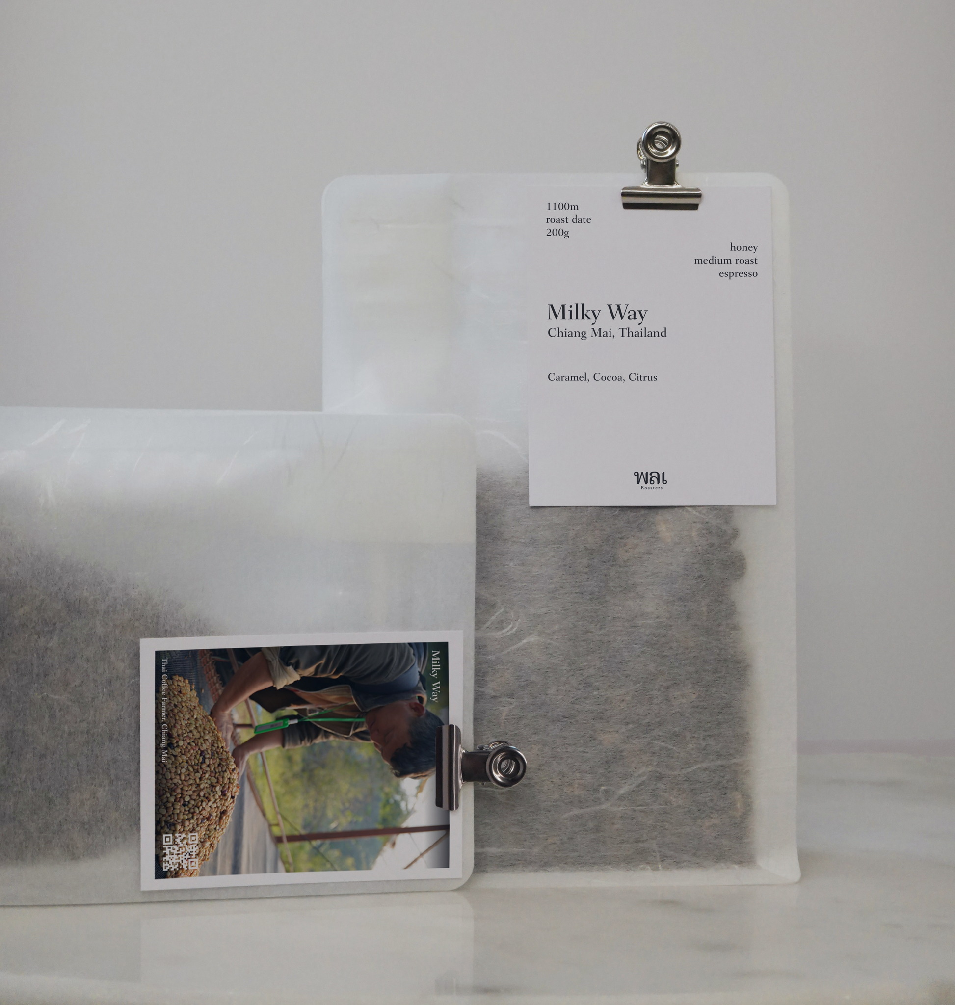 A clear/transparent/translucent bag of medium roast thai coffee beans from wai roasters with a card/postcard/polaroid clipped onto the bag roasted for espresso