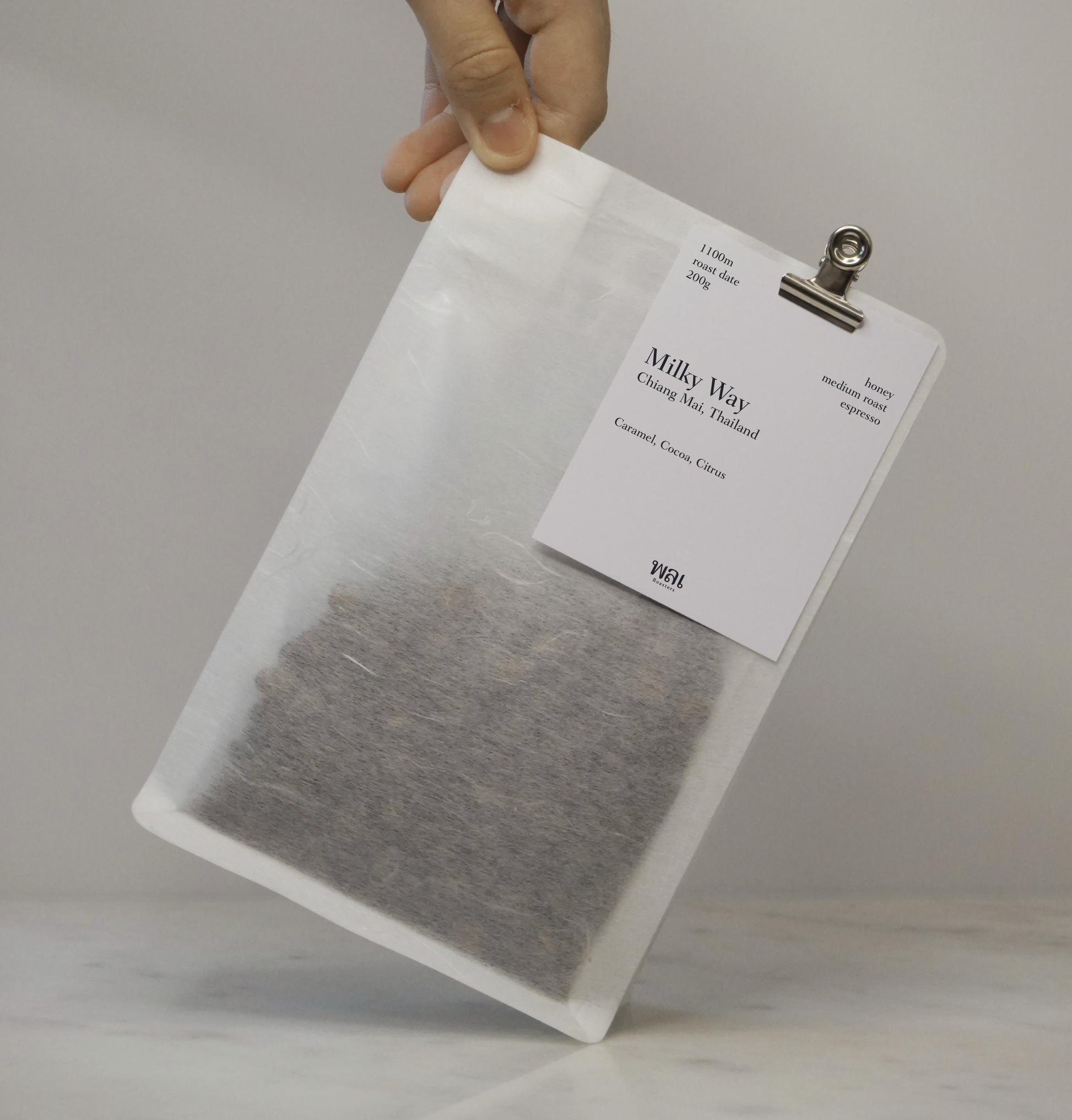 A clear/transparent/translucent bag of medium roast thai coffee beans from wai roasters with a card/postcard/polaroid clipped onto the bag roasted for espresso